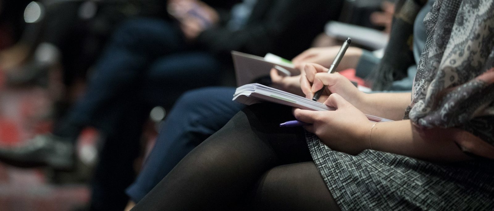 selective focus photography of people sitting on chairs while writing on notebooks